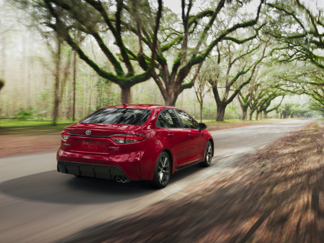 A red Toyota Corolla driving down a road with trees next to it