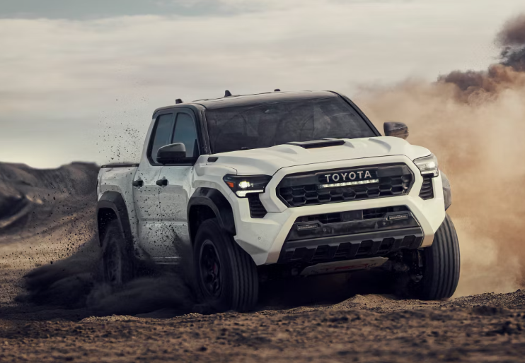 A white Toyota Tacoma driving in a dirt road