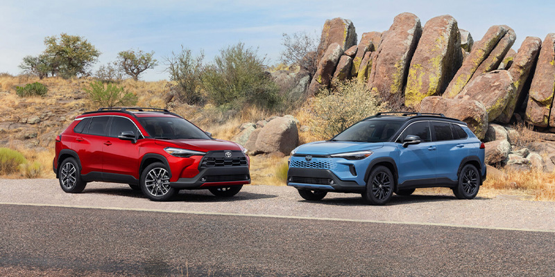 A red and a blue 2026 Toyota Corolla Cross parked side by side in a rugged outdoor setting.