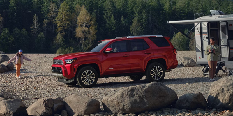 Red Toyota 4Runner parked by an RV in a forested, rocky landscape