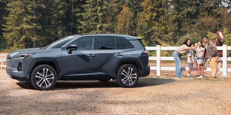 Gray Toyota SUV parked by a fence with a family petting a horse.